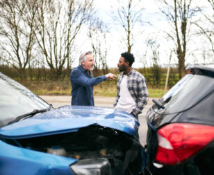 Two drivers arguing after a road rage car accident in Texas with damaged vehicles at the scene.