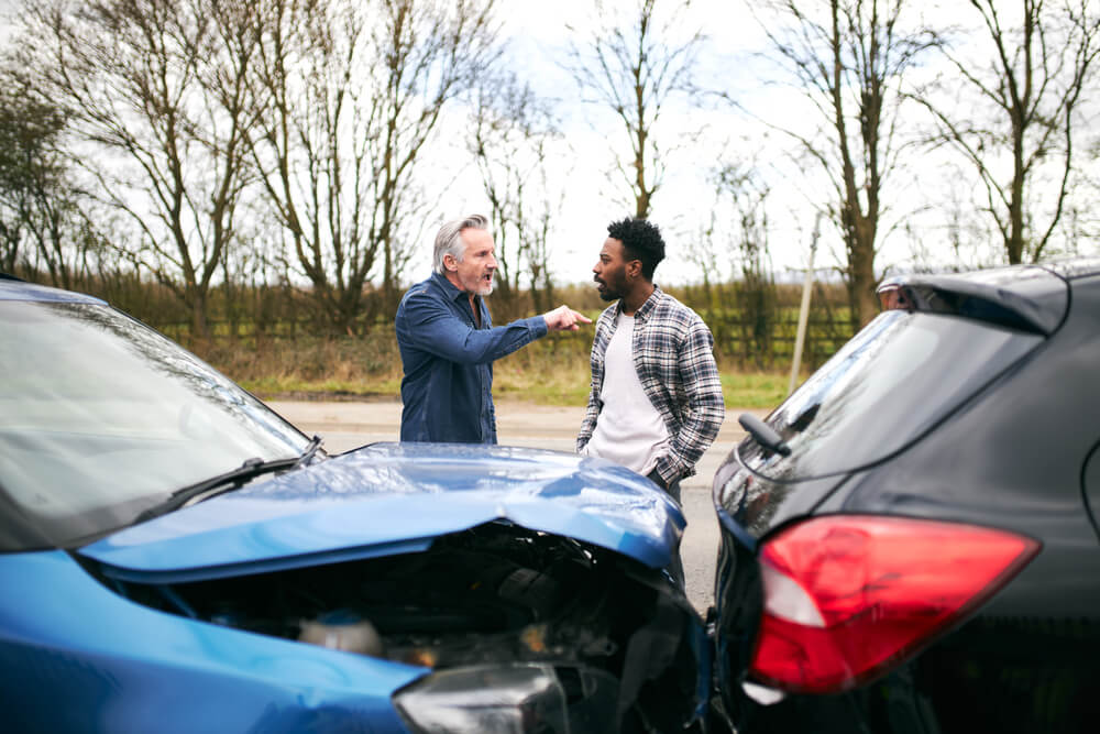 Two drivers arguing after a road rage car accident in Texas with damaged vehicles at the scene.