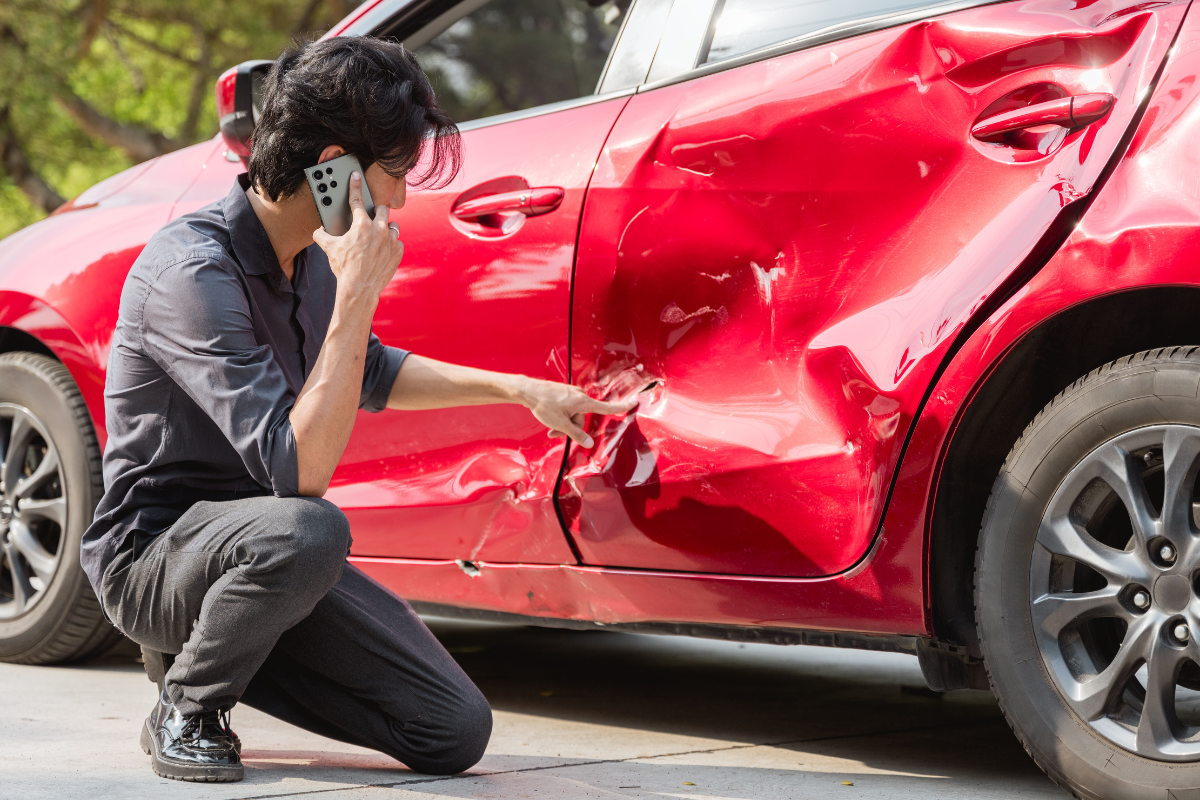 person kneeling beside damaged car